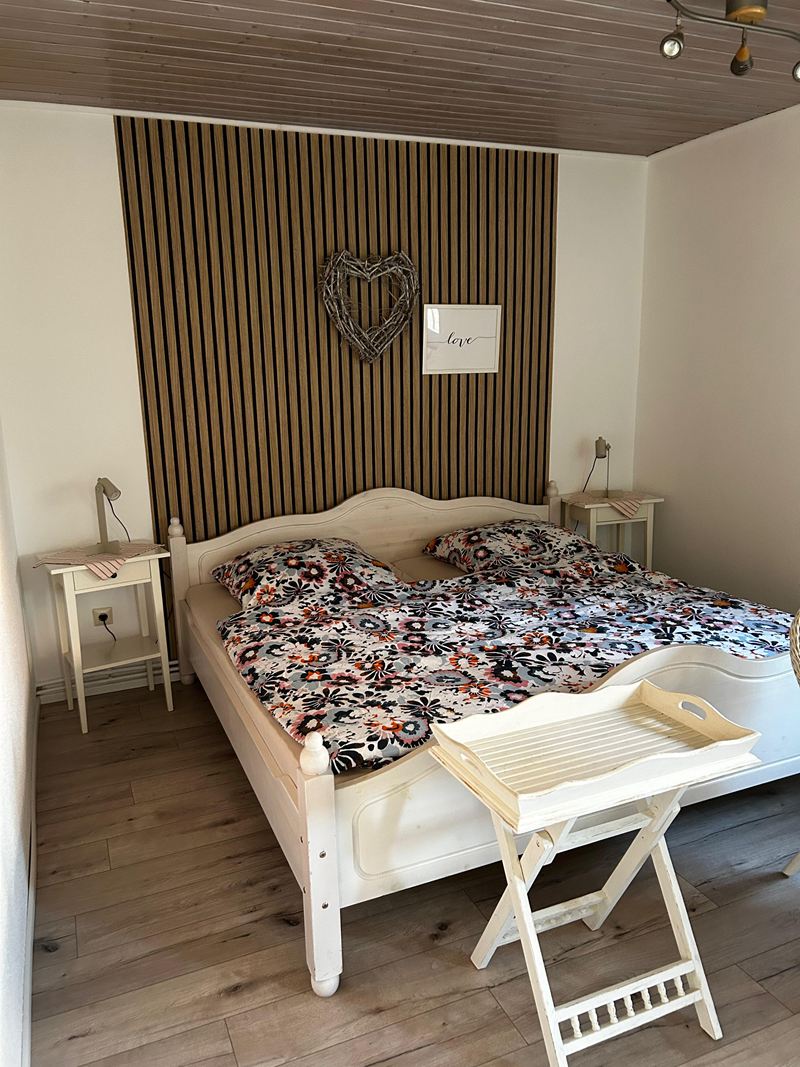 Schlafzimmer mit großem Bett und Holzlamellenwand in der Ferienwohnung Lilit