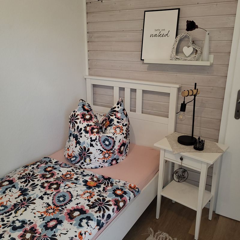 Bett mit geblümter Bettwäsche und Nachttischlampe in der Ferienwohnung Lotta
